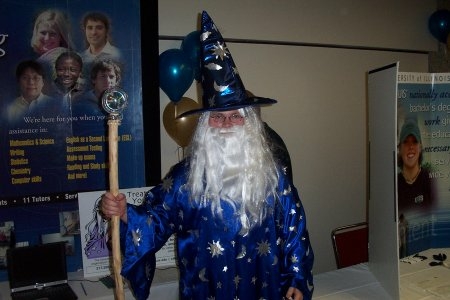 A person dressed as a wizard with a long white beard, a blue robe and hat with silver stars and moons holding a staff.